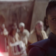 Reva holds a red lightsaber to Owen's neck as the people of Tatooine look on.